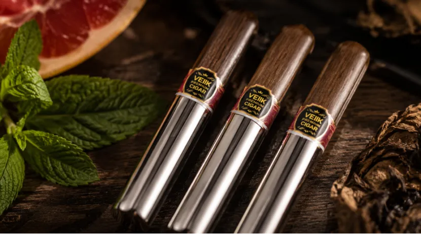 Three VEIIK cigar-shaped vapes on a wooden table with mint, grapefruit, and tobacco leaves